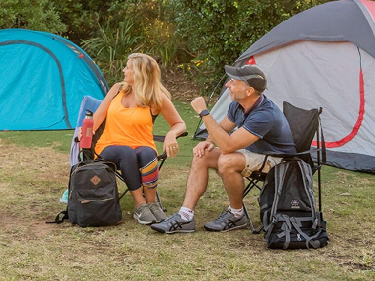2 campers sitting with their backpacks with their tents set up in the background. Photo: John