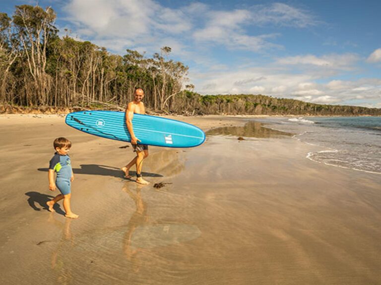 A father and young son head down to the water for a paddle, Woody Head campground, Bundjalung