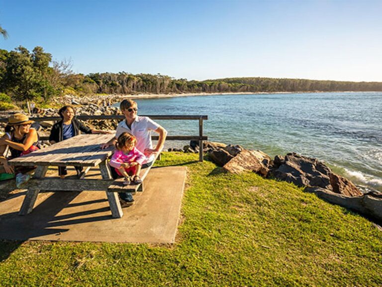 A group at a picnic table by the water, Woody Head campground, Bundjalung National Park. Photo: John